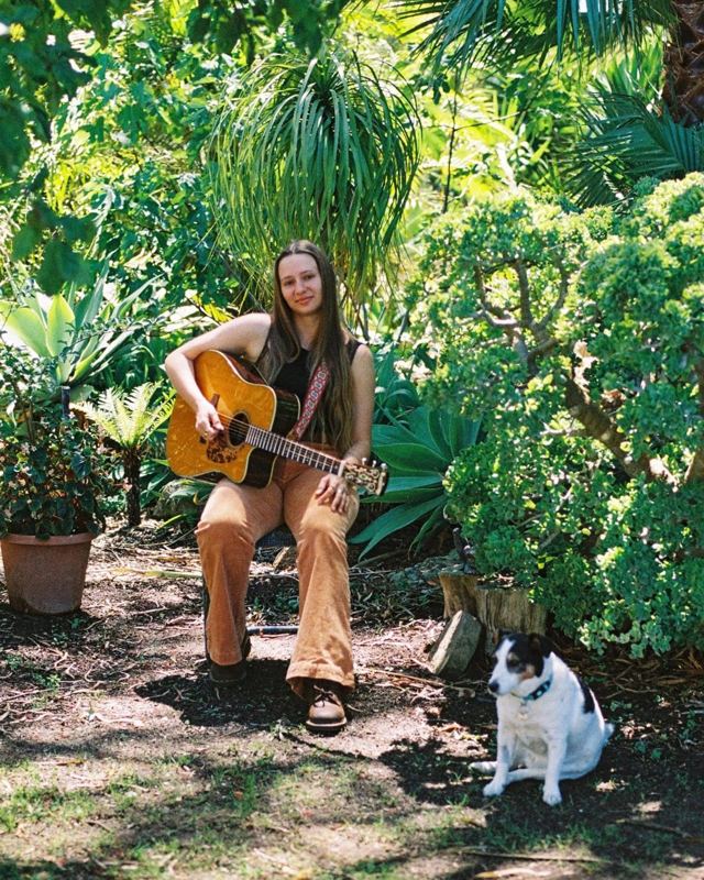 Savanah Solomon with her guitar in a garden, a dog sitting nearby